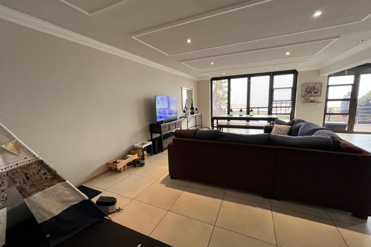 Spacious living area featuring large glass sliding doors, recessed ceiling detailing with downlights, and neutral tiled flooring.