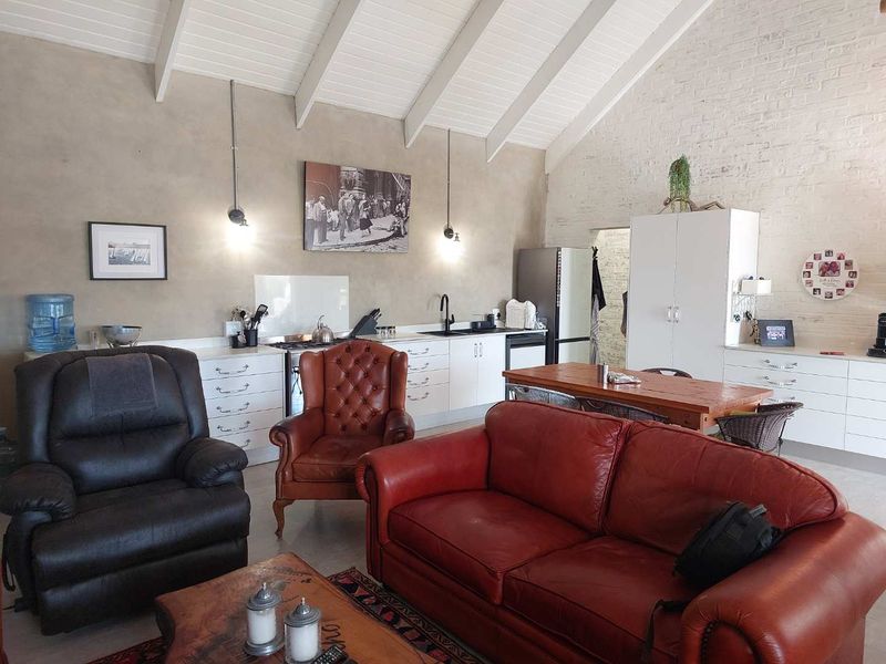 Spacious open-plan living area featuring a vaulted ceiling with exposed rafters, a textured brick wall, and a functional kitchen with built-in cabinetry.