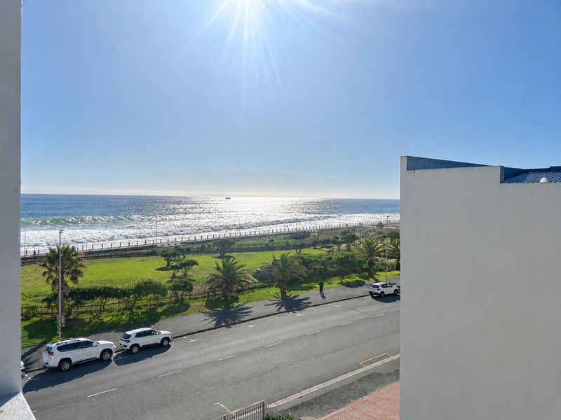 A scenic elevated view overlooking the coastal road, green parkland, and the ocean horizon.