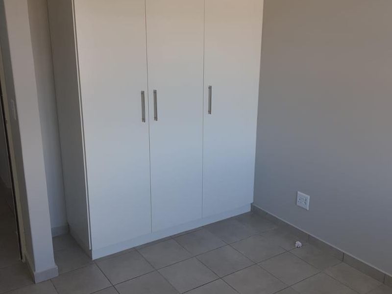 A clean, empty bedroom featuring neutral wall paint, tiled flooring, and a modern white built-in wardrobe.