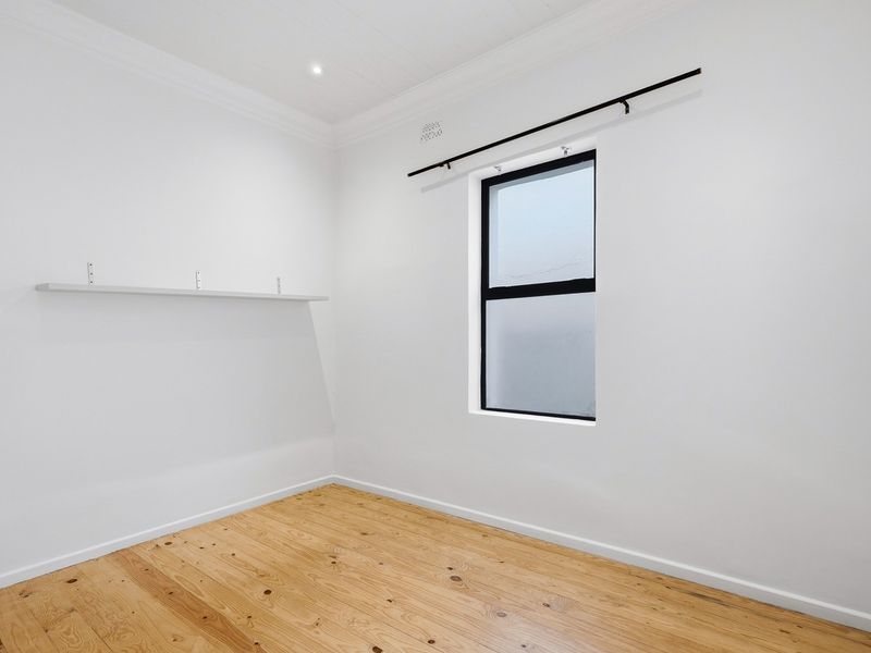 A bright, empty bedroom featuring polished timber flooring, a frosted glass window, and neutral white walls, ready for personalization.