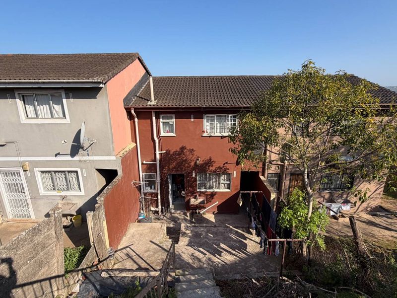 Rear view of a multi-story townhouse featuring a concrete courtyard, external stairs, and weathered exterior finishes.