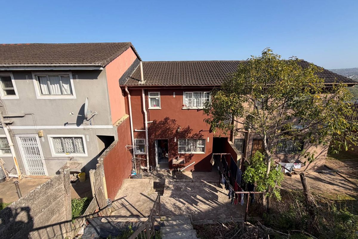 Rear view of a multi-story townhouse featuring a concrete courtyard, external stairs, and weathered exterior finishes.