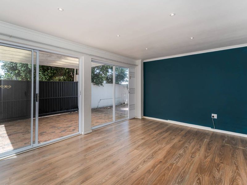 Bright and spacious living area featuring laminate flooring, recessed lighting, and large sliding glass doors that open onto a paved patio area.