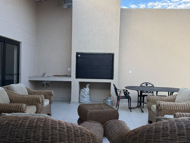 Covered patio area featuring a built-in braai, concrete prep counter with sink, and tiled flooring, providing a functional outdoor entertainment space.