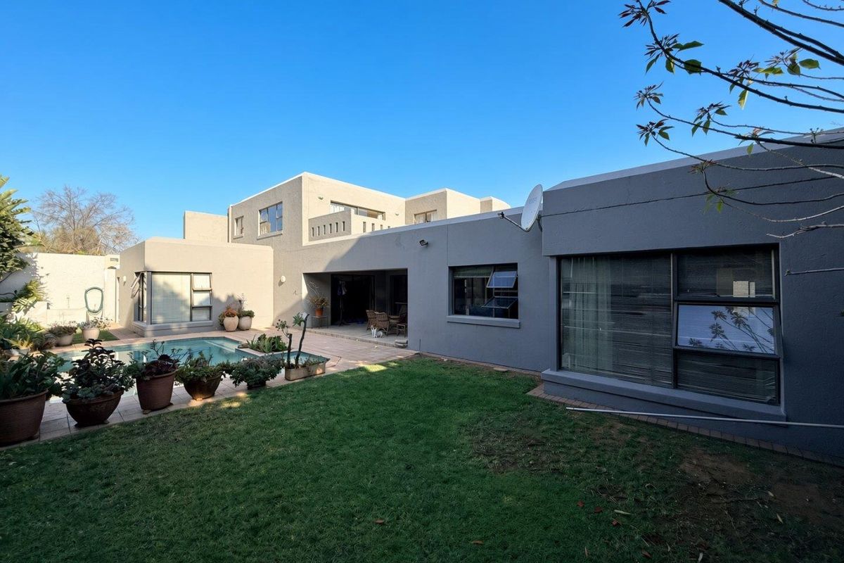 Rear view of the property featuring a swimming pool, paved patio area, and a well-maintained lawn set against the modern building facade.