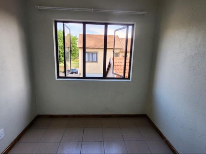 An empty bedroom featuring tiled flooring, neutral walls, and an aluminium window frame with a curtain rail.