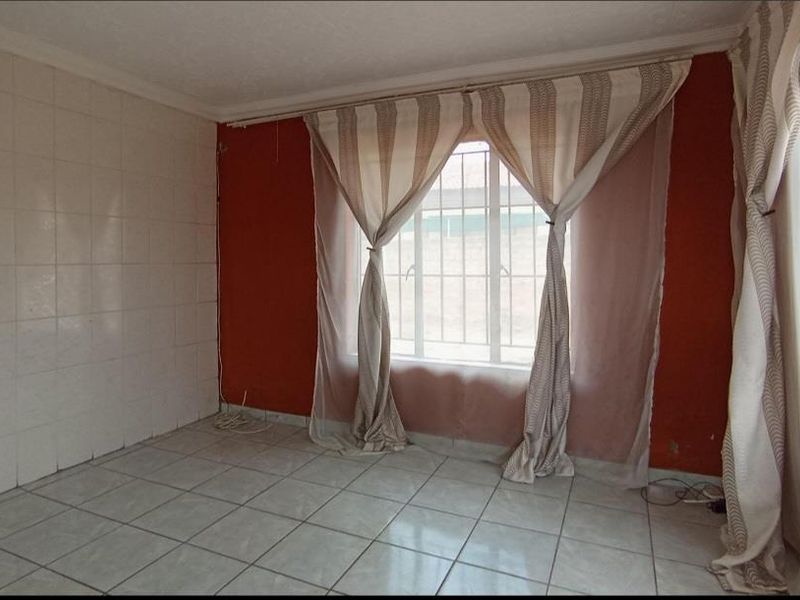 An empty living area featuring tiled flooring, a tiled accent wall, and security bars on the window, ready for a modern update.