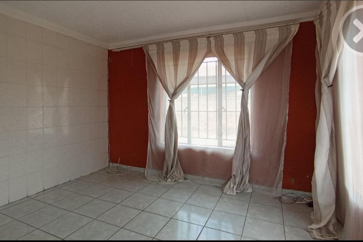 An empty living area featuring tiled flooring, a tiled accent wall, and security bars on the window, ready for a modern update.
