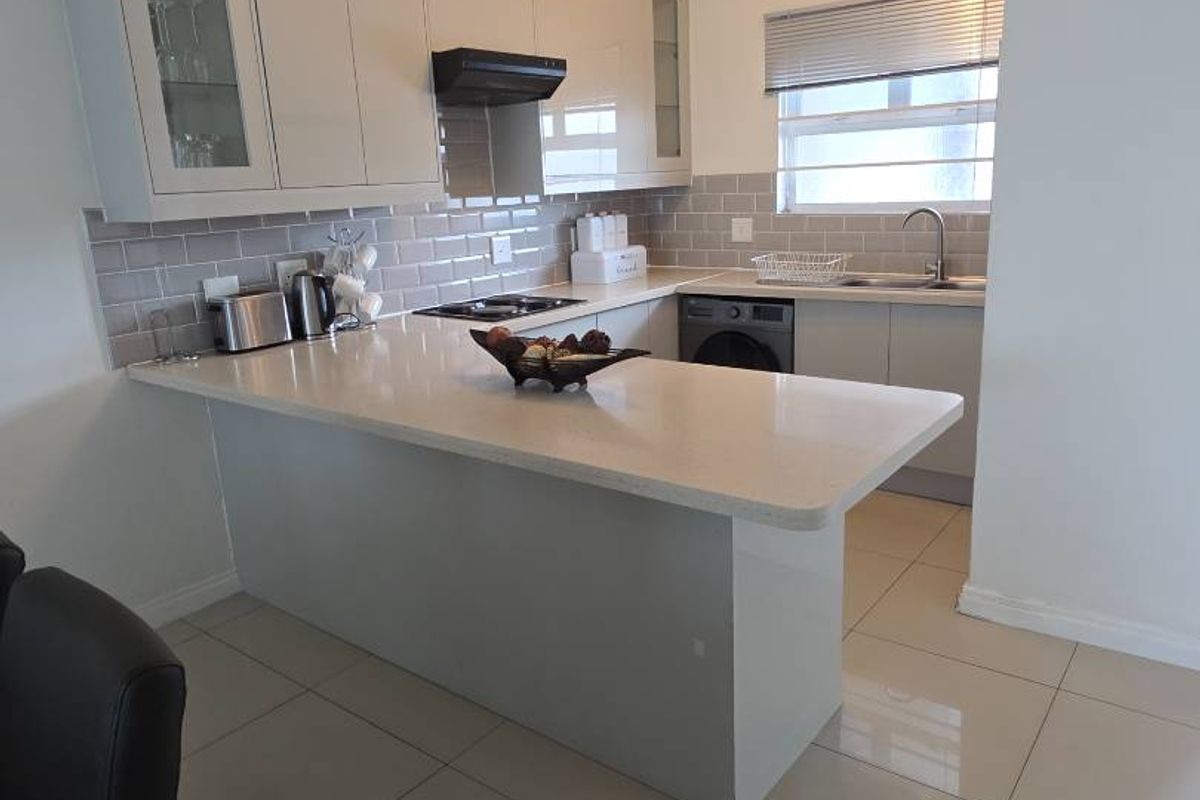 Modern kitchen featuring sleek cabinetry, stone countertops, a breakfast bar, subway tile backsplash, and integrated appliances, finished with polished floor tiles.
