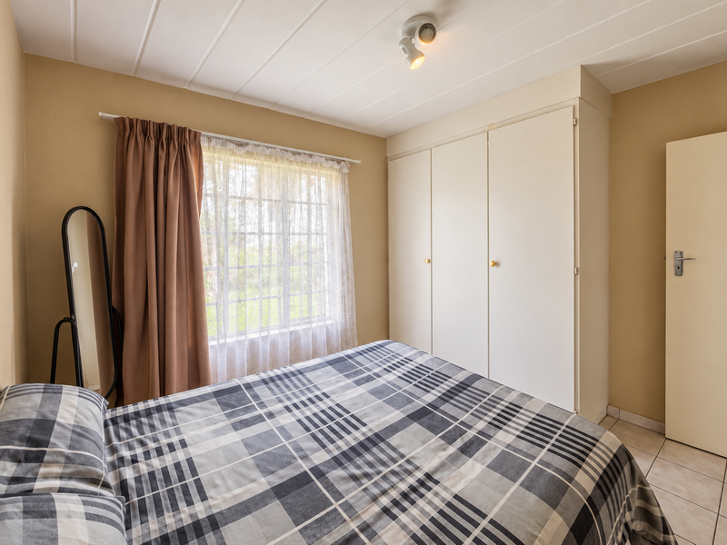 A functional bedroom featuring built-in wardrobes, tiled flooring, and a window with curtains, providing a neutral space ready for personalization.