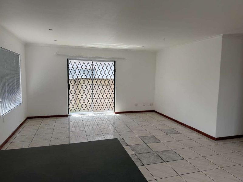 An empty, open-plan living area featuring tiled flooring, recessed lighting, and a sliding glass door with a security gate leading to the exterior.