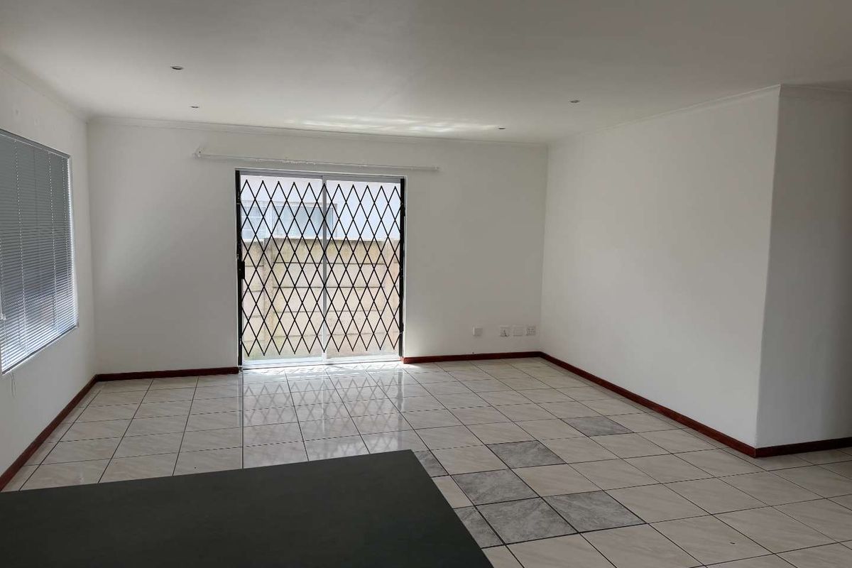 An empty, open-plan living area featuring tiled flooring, recessed lighting, and a sliding glass door with a security gate leading to the exterior.