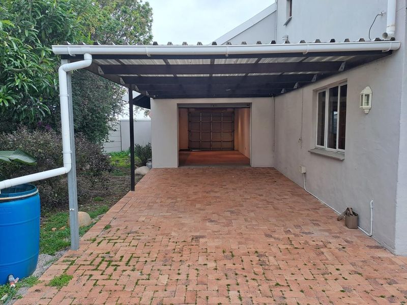 A covered carport area with brick paving leading to a single garage, featuring a functional gutter system and exterior lighting.