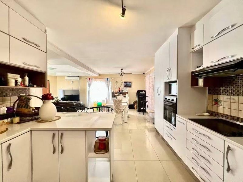 Open-plan kitchen and living area featuring white cabinetry, integrated appliances, tiled flooring, and a seamless flow between the cooking and lounge spaces.