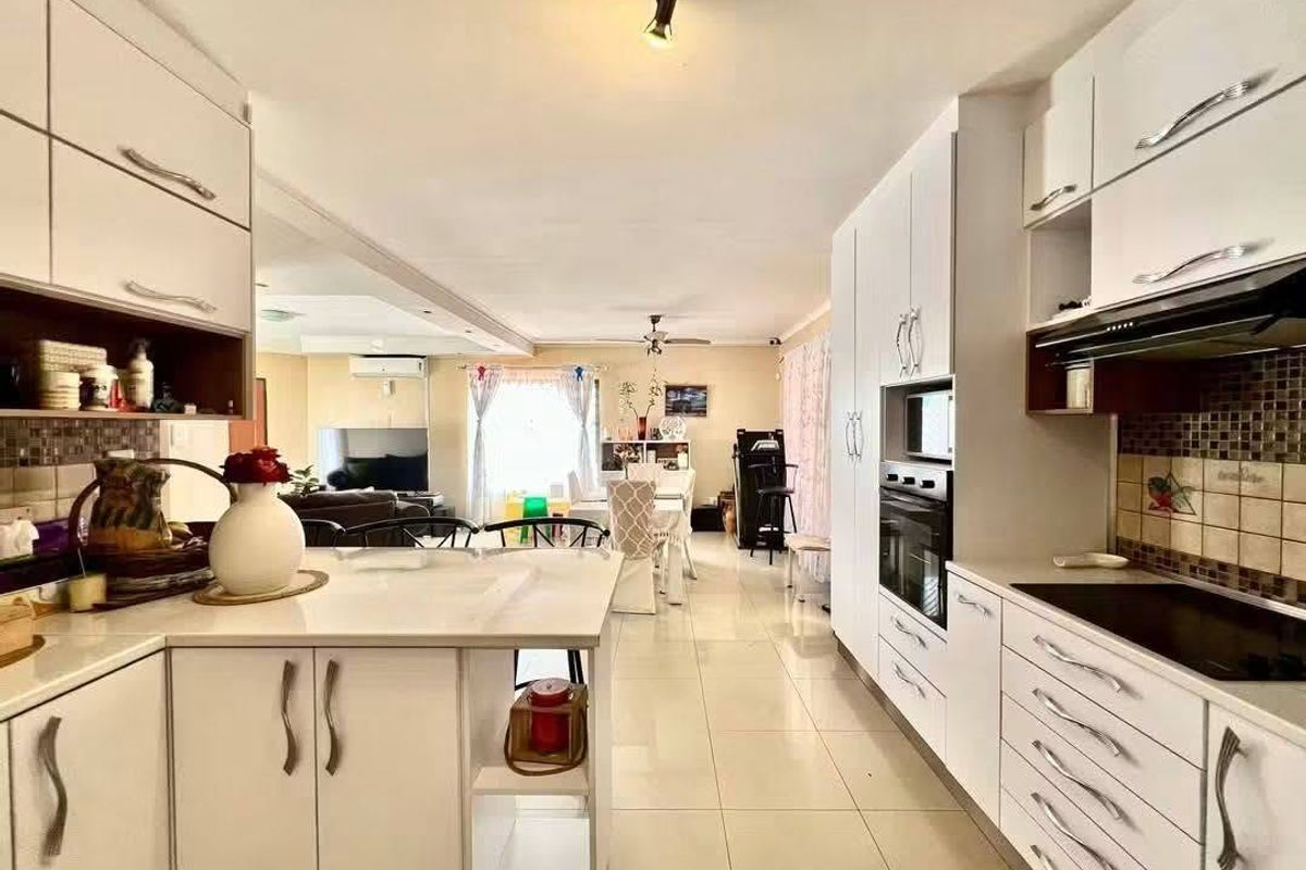 Open-plan kitchen and living area featuring white cabinetry, integrated appliances, tiled flooring, and a seamless flow between the cooking and lounge spaces.