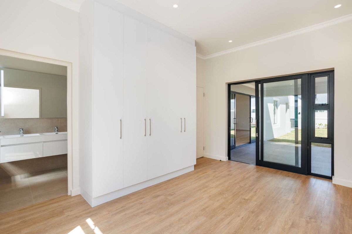 A bright bedroom featuring built-in wardrobes, wood-look flooring, recessed lighting, and sliding glass doors leading to an outdoor patio, with an en-suite bathroom.