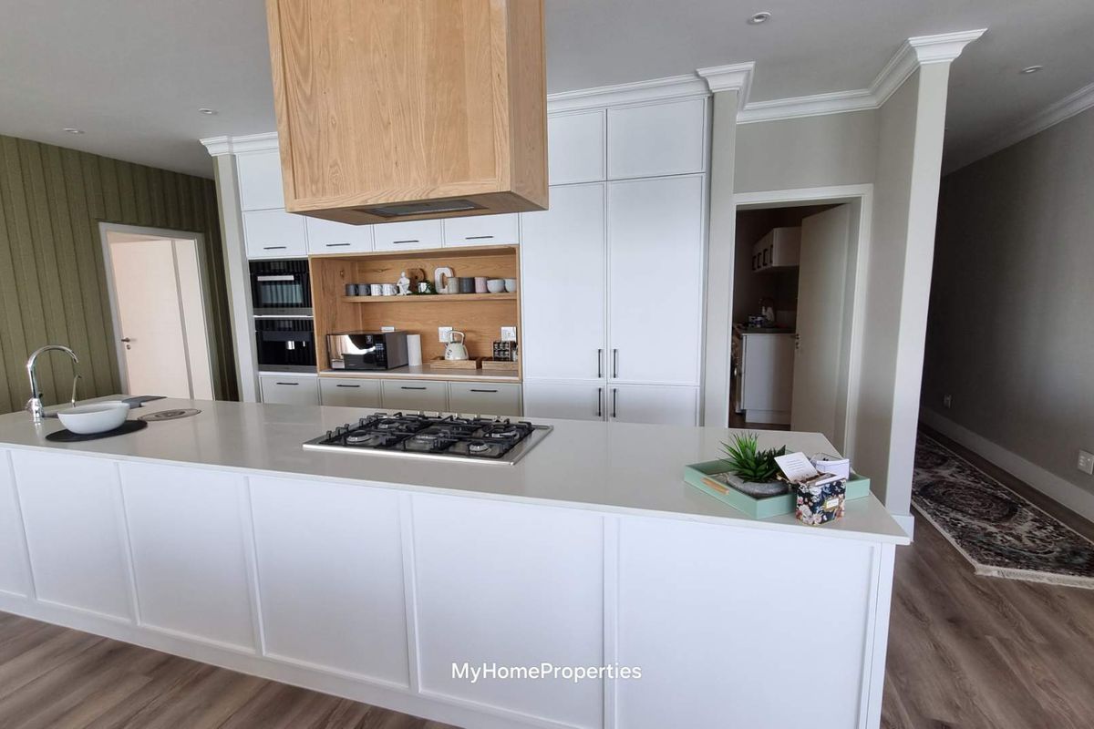 Modern kitchen featuring a large central island with a gas cooktop, integrated appliances, and sleek white cabinetry with wood accents.