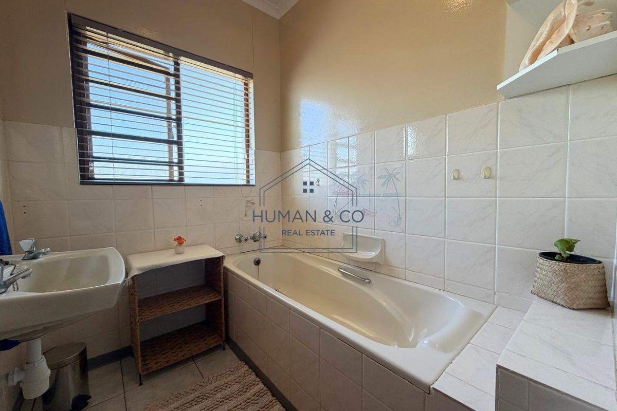A functional bathroom featuring a built-in bathtub, wall-mounted basin, and tiled wall finishes, offering a clean and practical space.