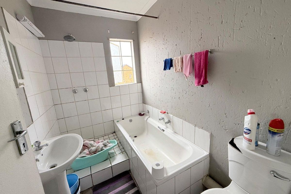 A functional bathroom featuring a standard bathtub, pedestal basin, and toilet with tiled splashbacks and textured wall finishes.