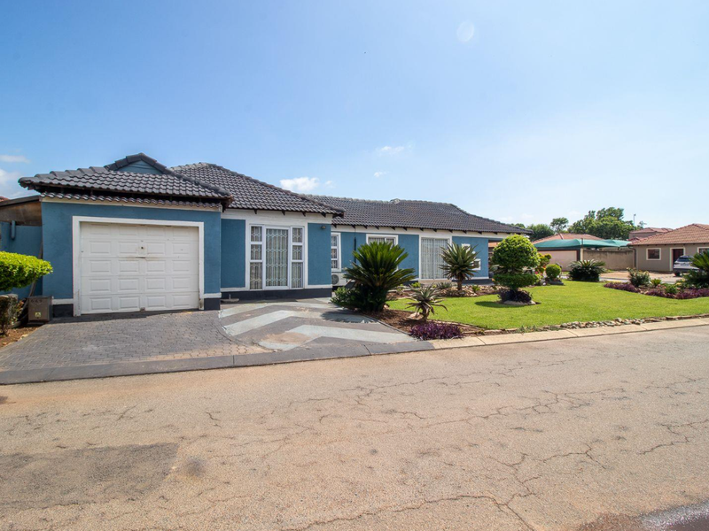 Front view of a single-story house featuring a tiled roof, attached garage, paved driveway, and a well-maintained front garden.