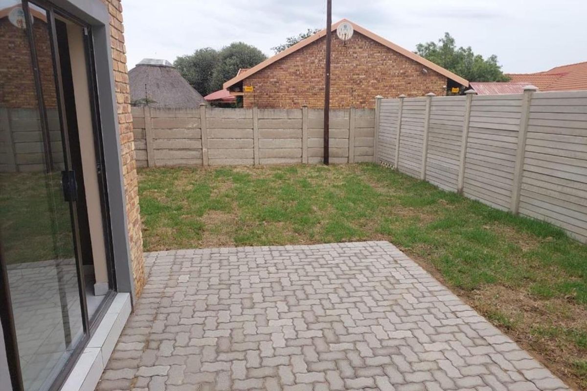 A private rear garden featuring a paved patio area, lawn, and secure precast concrete boundary walls, accessible via a sliding glass door.