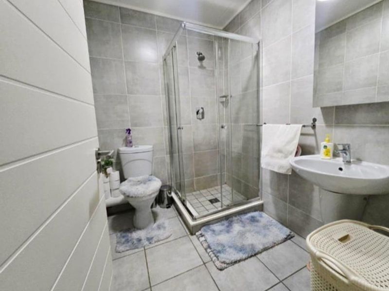 A functional bathroom featuring a glass shower enclosure, pedestal basin, and toilet with neutral wall and floor tiling.
