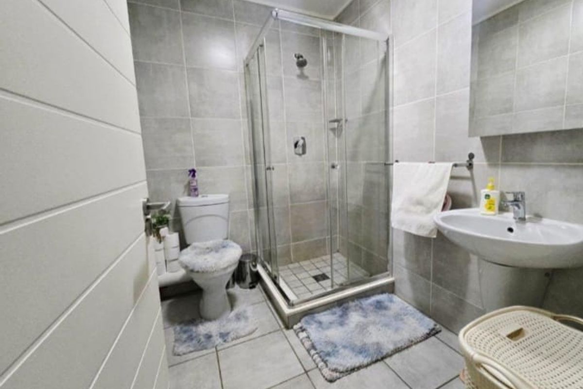 A functional bathroom featuring a glass shower enclosure, pedestal basin, and toilet with neutral wall and floor tiling.