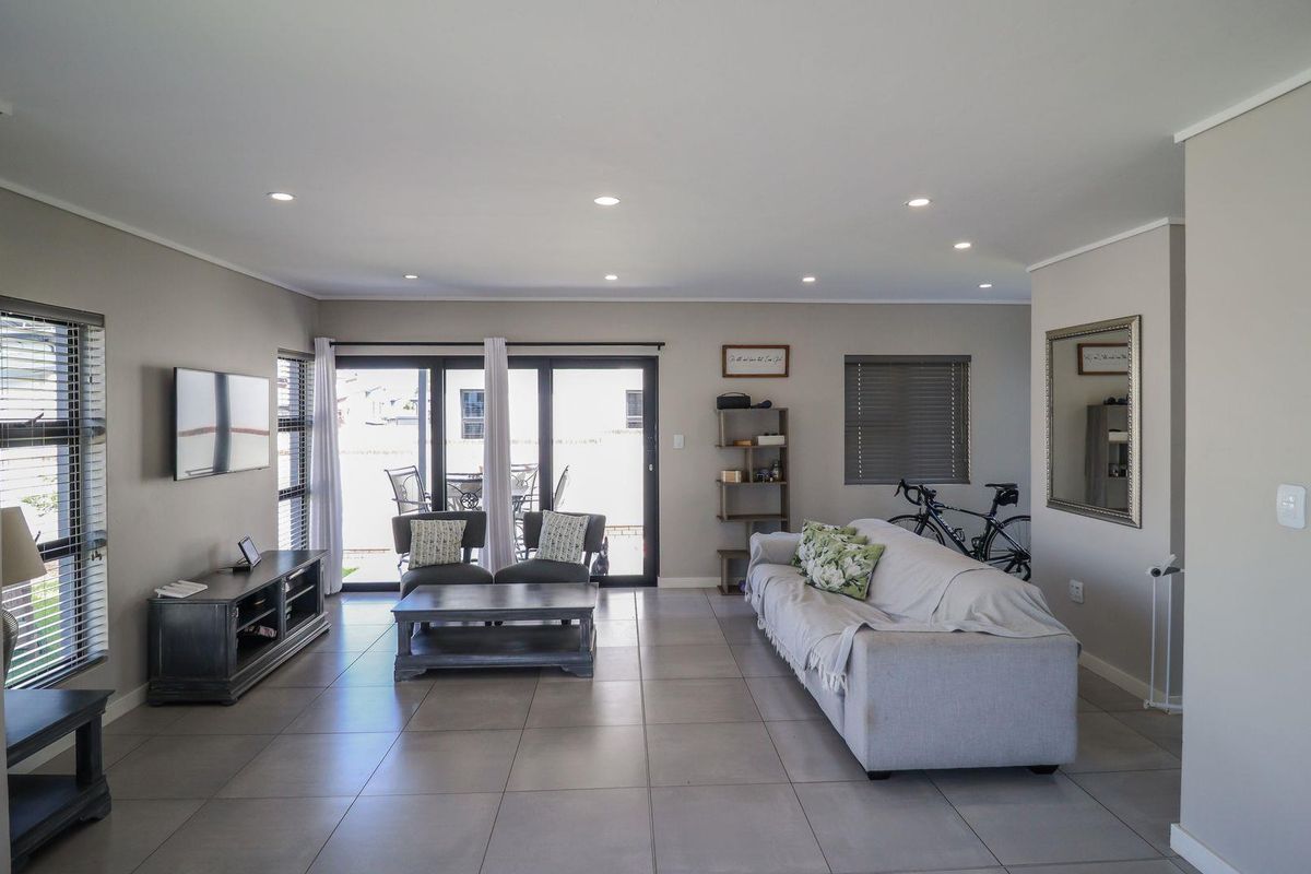 Spacious living room featuring neutral tiled flooring, recessed downlighting, and large sliding glass doors providing access to the outdoor patio area.