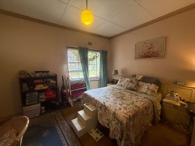 A bedroom featuring a built-in headboard, security bars on the window, and dated ceiling tiles, offering potential for a modern cosmetic update.