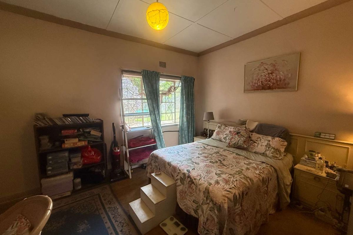 A bedroom featuring a built-in headboard, security bars on the window, and dated ceiling tiles, offering potential for a modern cosmetic update.
