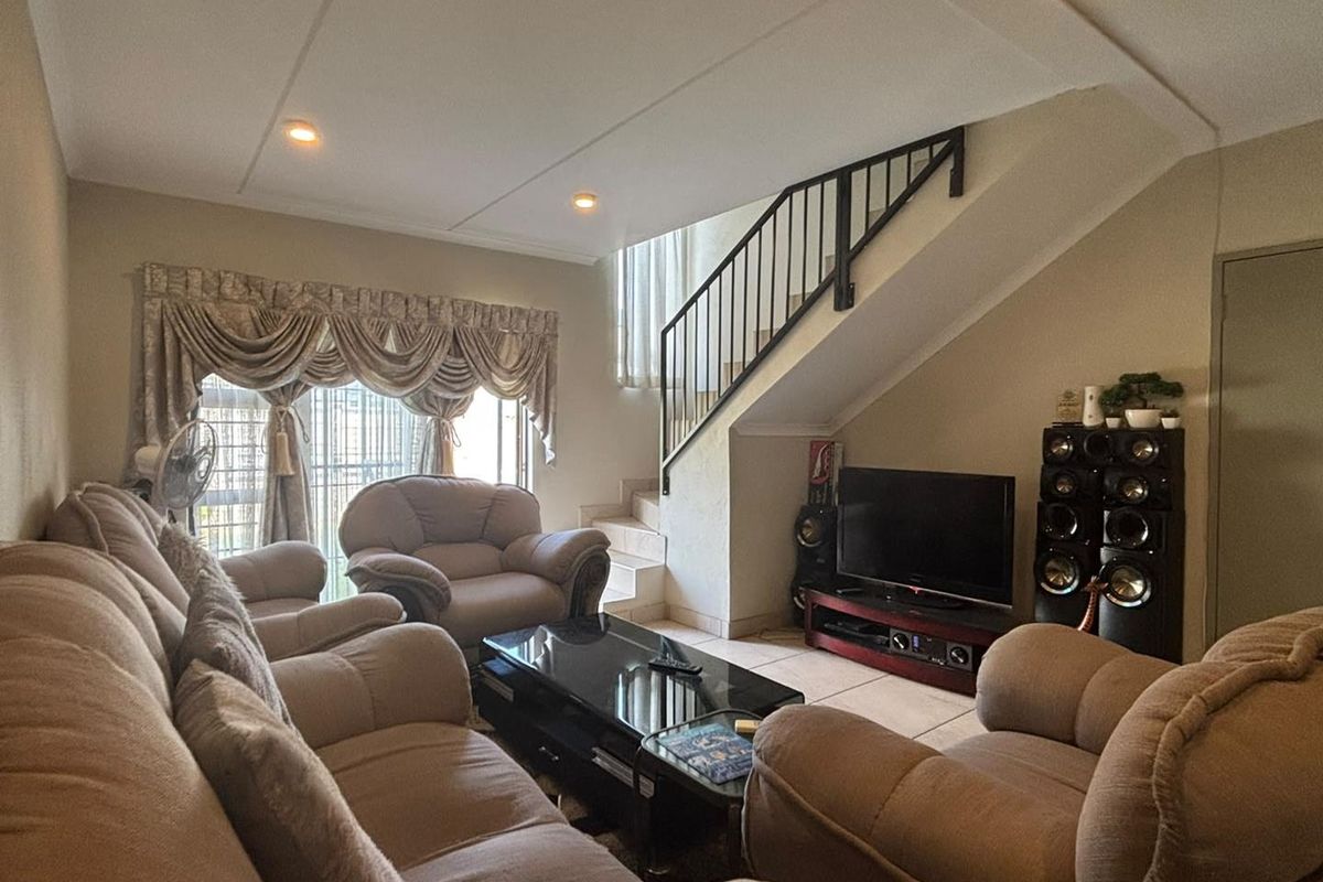 A comfortable living room featuring tiled flooring, recessed lighting, and an internal staircase with a metal balustrade.