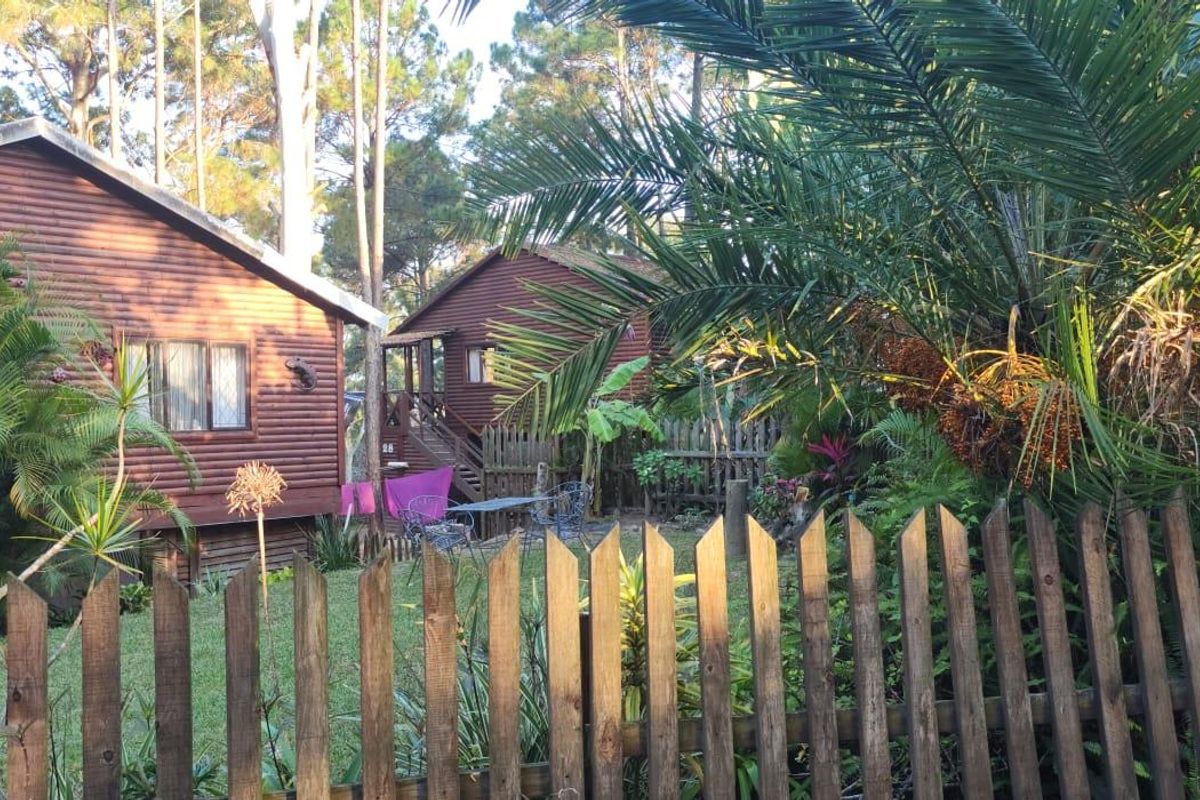 A view of timber log cabins set within a lush, landscaped garden, featuring a wooden picket fence and elevated outdoor decking.