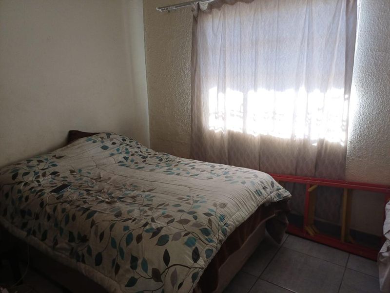 A bedroom featuring tiled flooring and a window with a curtain rail, requiring cosmetic updates to the wall finishes.