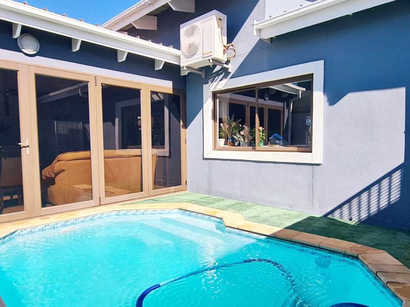 A well-maintained outdoor pool area featuring a compact swimming pool, modern sliding glass doors, and an exterior air conditioning unit.