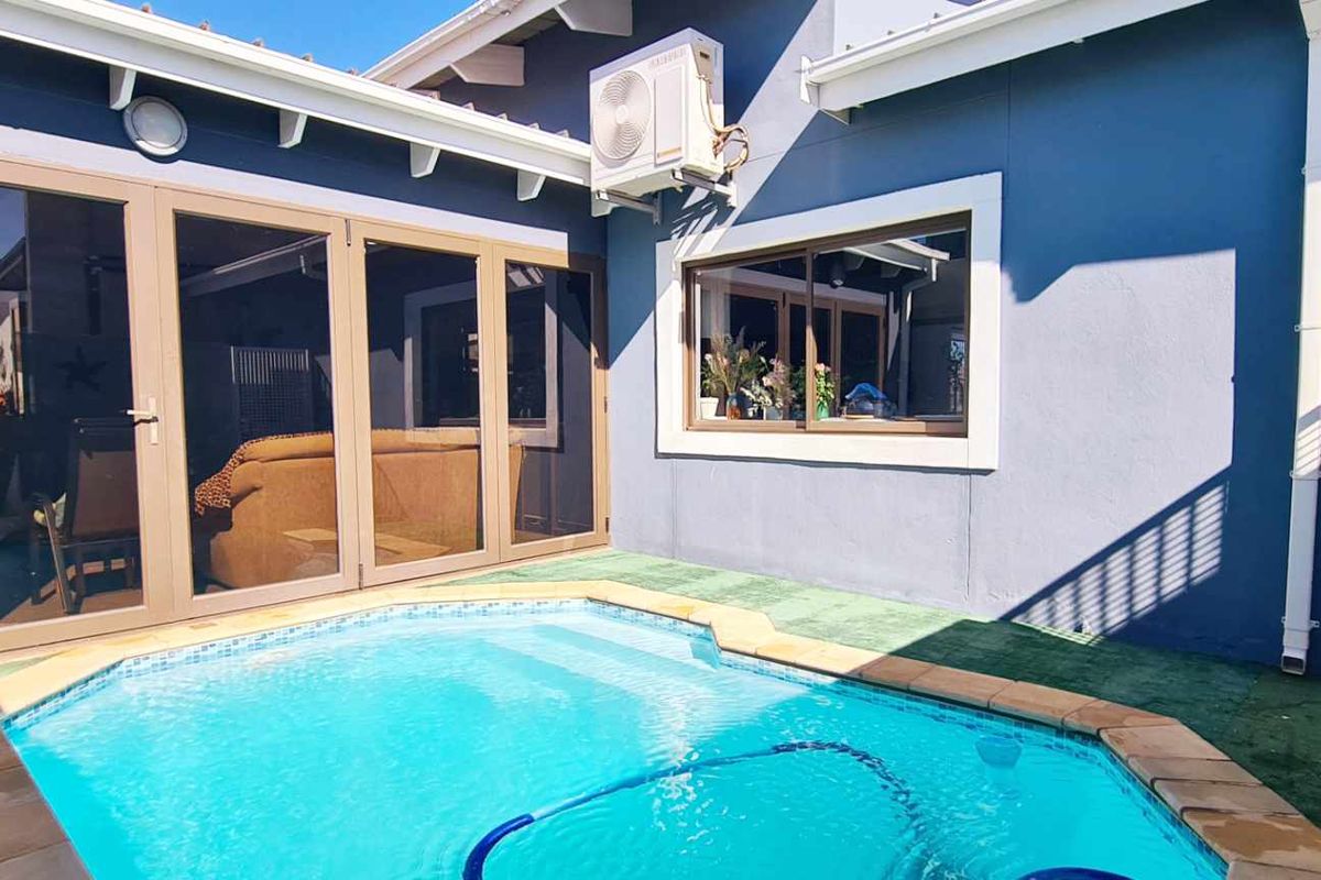 A well-maintained outdoor pool area featuring a compact swimming pool, modern sliding glass doors, and an exterior air conditioning unit.