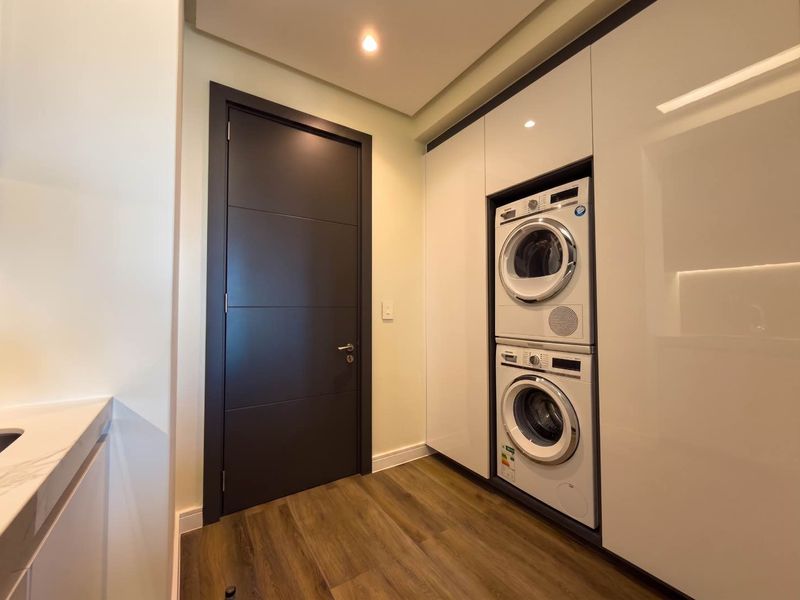 Modern laundry room featuring sleek built-in cabinetry and a stacked washer-dryer unit, finished with high-quality flooring and recessed lighting.