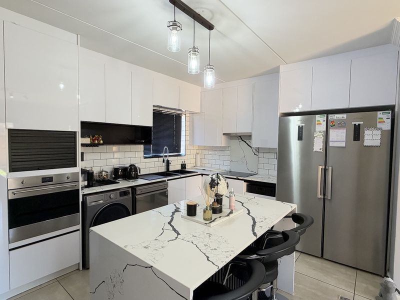 Modern kitchen featuring high-gloss white cabinetry, marble-look island countertop, subway tile backsplash, and integrated appliances with contemporary pendant lighting.
