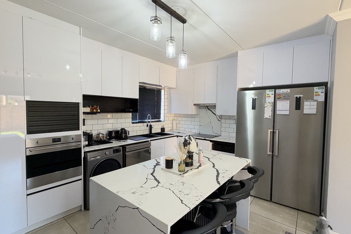 Modern kitchen featuring high-gloss white cabinetry, marble-look island countertop, subway tile backsplash, and integrated appliances with contemporary pendant lighting.