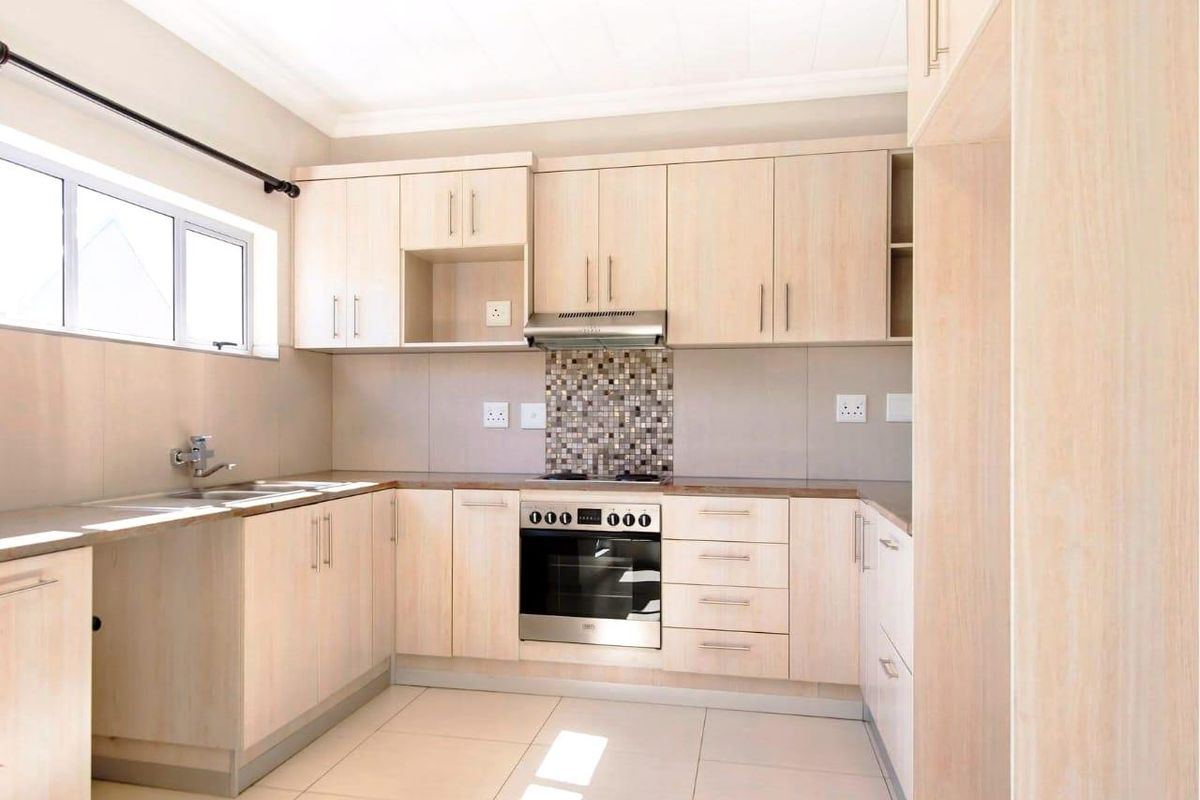 A modern kitchen featuring light wood cabinetry, a built-in oven, extractor fan, mosaic tile backsplash, and tiled flooring.