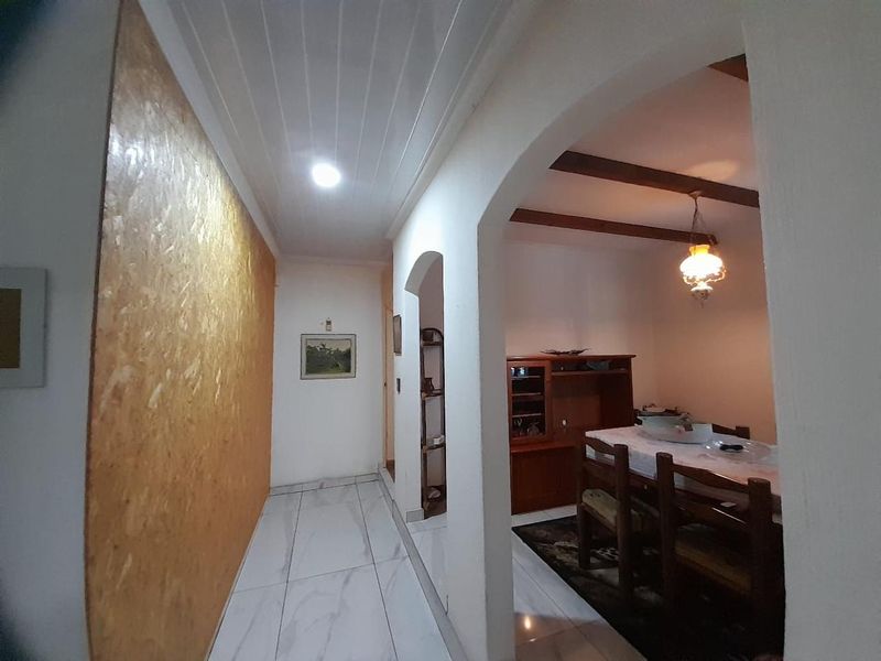 A hallway featuring tiled flooring and timber ceiling paneling, leading through an arched doorway into an adjacent dining area with exposed timber beams.