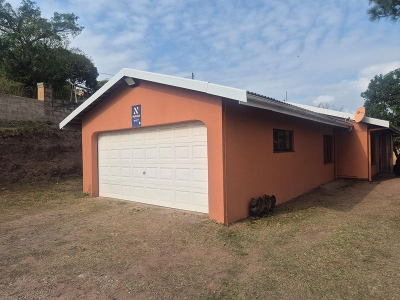 A detached single garage with a white sectional door and terracotta-colored exterior walls, situated on a grass and dirt lot.