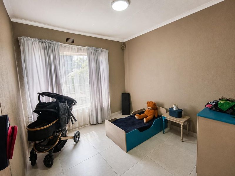 A bedroom featuring tiled flooring, neutral wall paint, and a window with security bars, providing a functional space for a child's room.