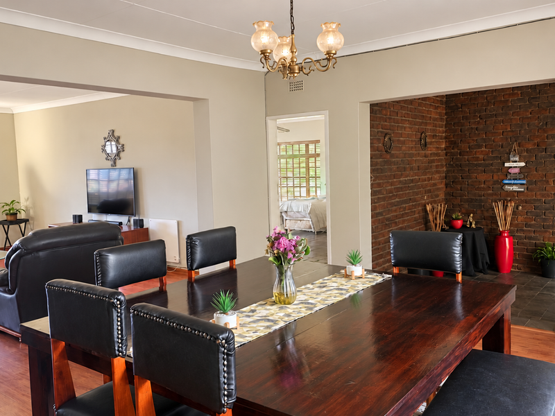 Spacious open-plan living and dining area featuring warm laminate flooring, a striking exposed brick feature wall, and elegant coved ceilings.
