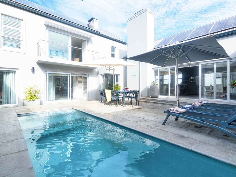 A well-maintained outdoor pool area featuring a stone patio, integrated swimming pool, and direct access to the home through large sliding glass doors.