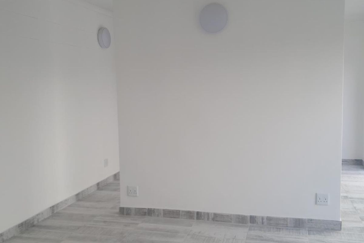 A bright, empty living area featuring modern wood-look tiled flooring, neutral white walls, and flush-mount lighting fixtures.