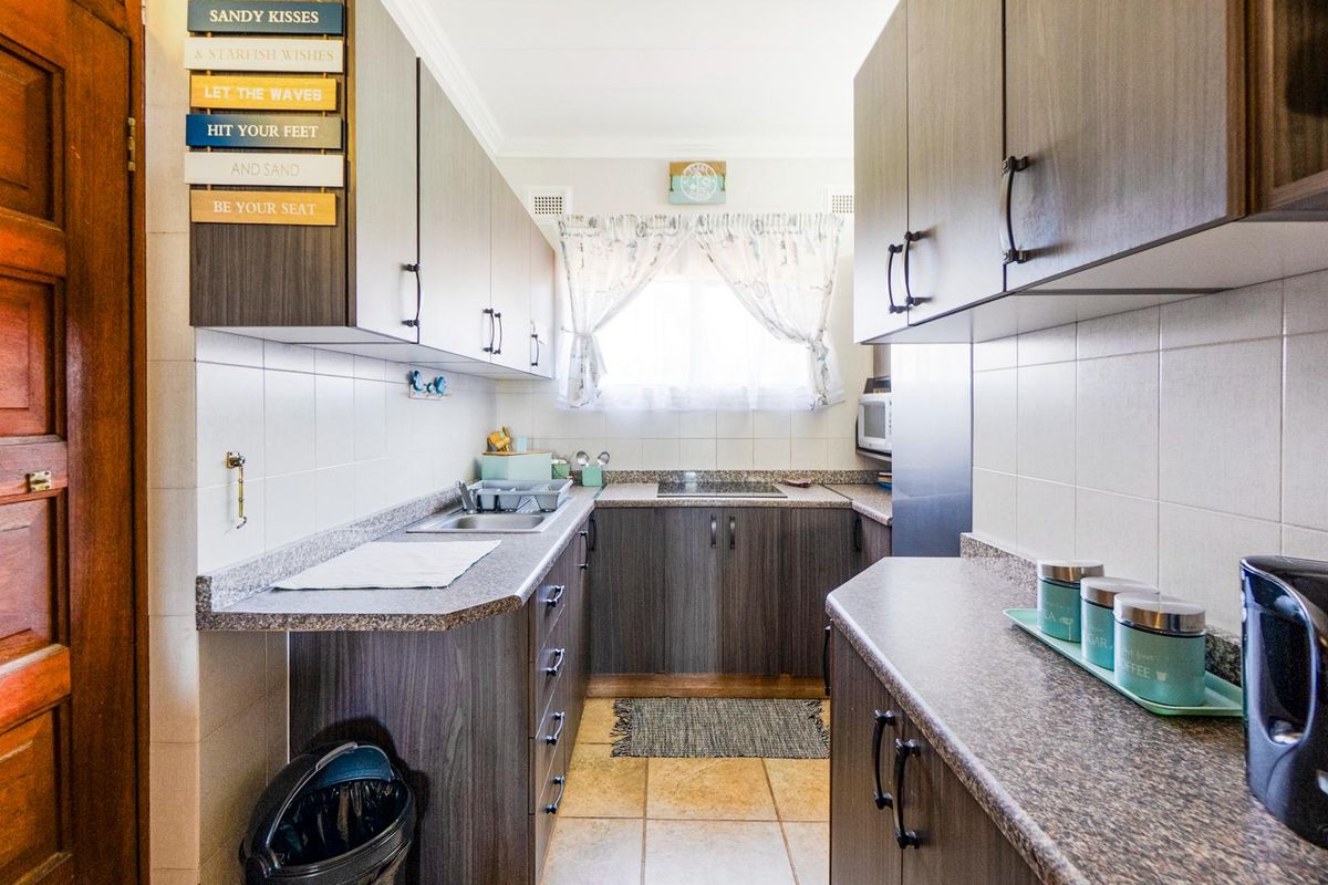 A functional galley-style kitchen featuring dark wood-grain cabinetry, laminate countertops, tiled splashbacks, and tiled flooring.