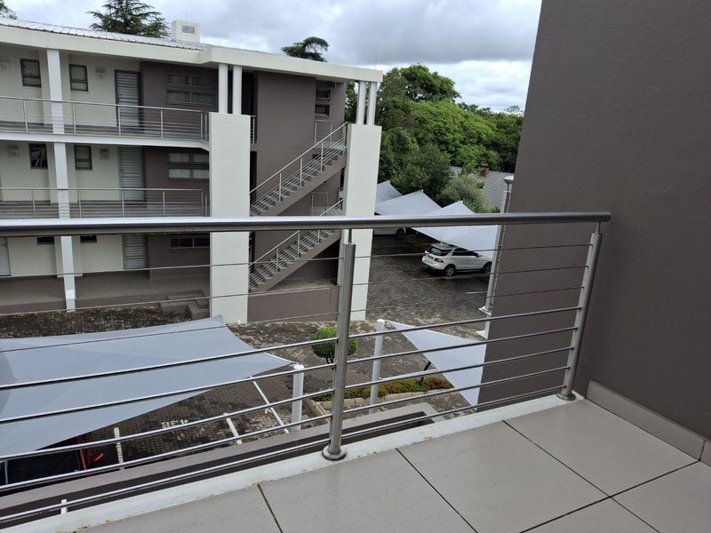A modern apartment balcony featuring a stainless steel balustrade and tiled flooring, overlooking the complex parking area and external stairwell.