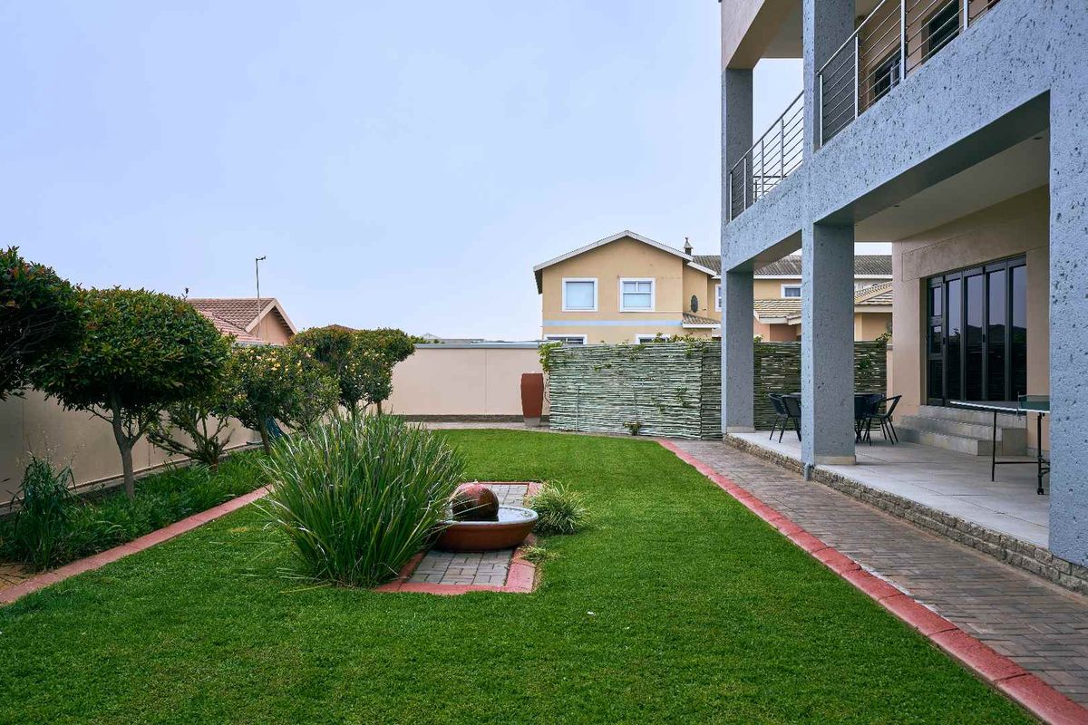 A well-maintained rear garden featuring a manicured lawn, a central water feature, and a covered patio area adjacent to the main house structure.