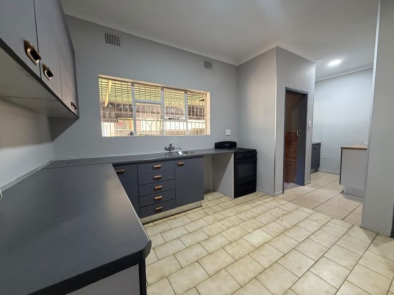 A functional kitchen featuring grey cabinetry, laminate countertops, a freestanding stove, and tiled flooring, offering a clean and practical workspace.
